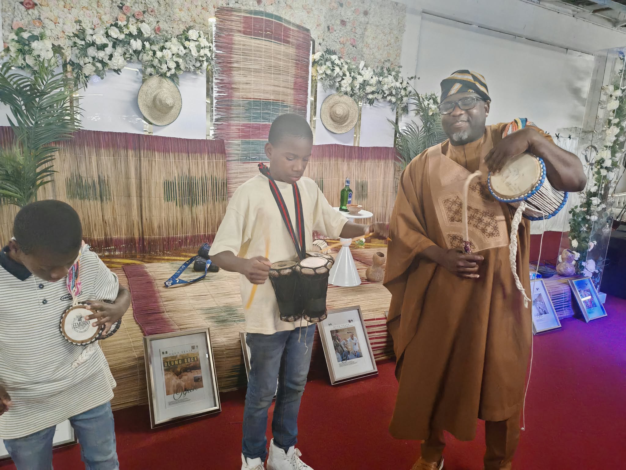 Sunday Abidemi Ipadeola in Agbada teaching young boys drumming at a traditional cultural exhibition